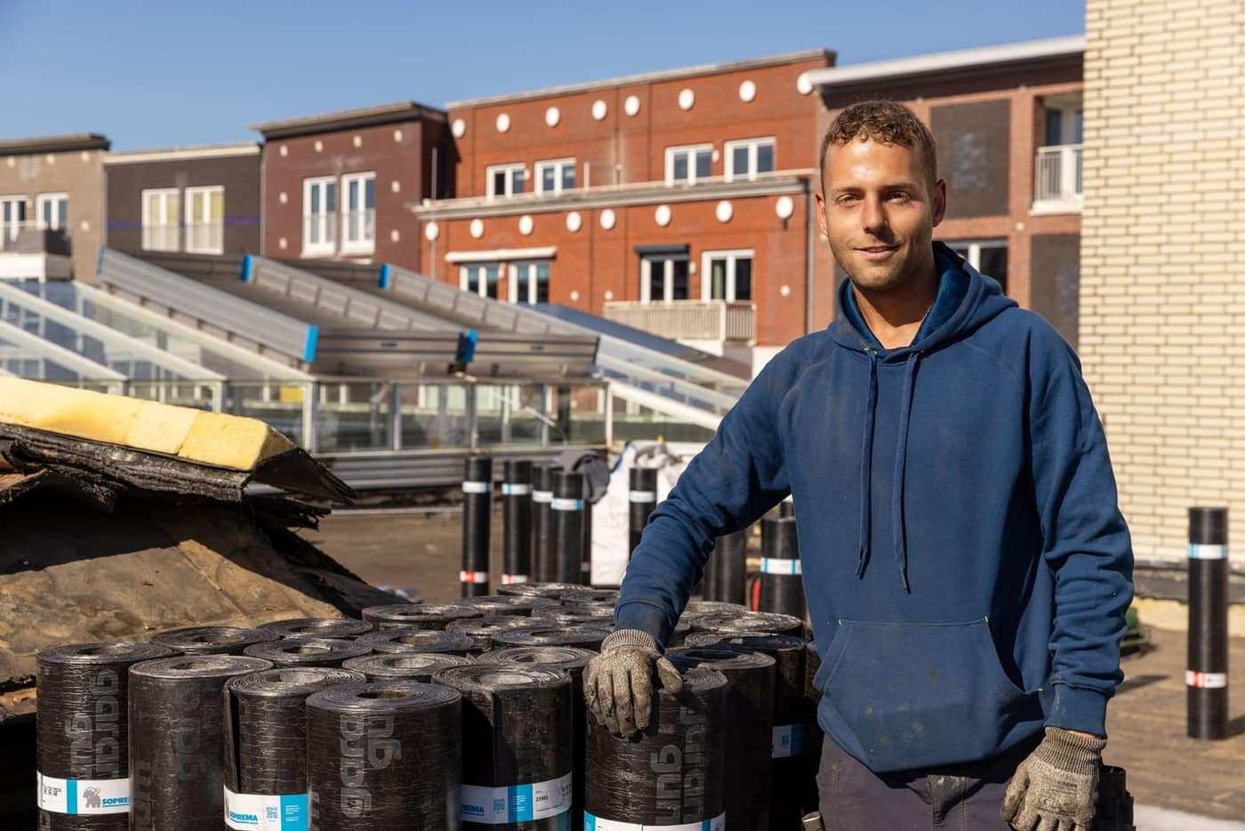 Dakdekker van Premium Dakwerken op een plat dak, naast de bitumenrollen voor het werk van die dag.