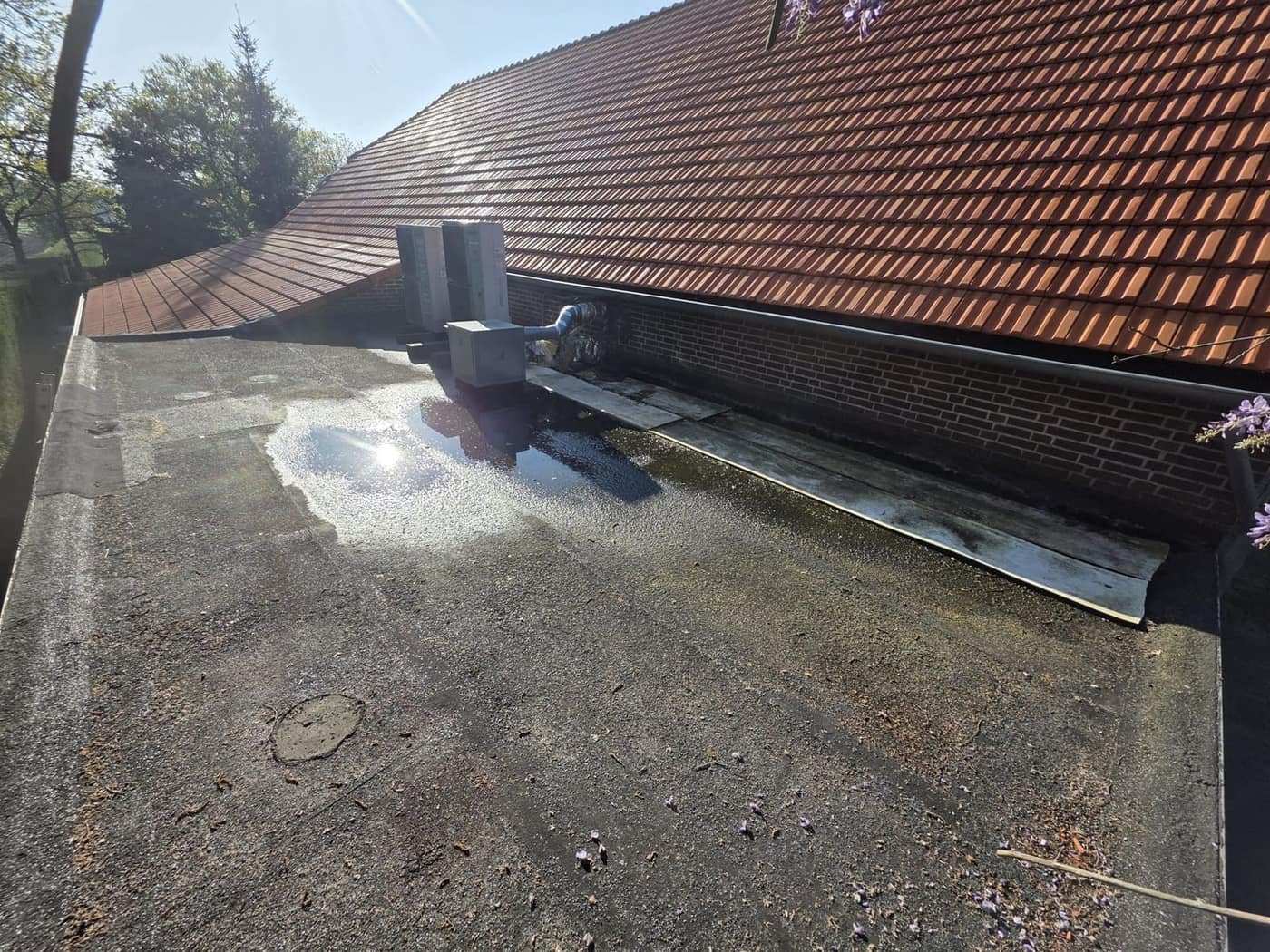 Plat dak langs een pannendak met stilstaand water bij de afvoer, gezien tijdens een inspectie.