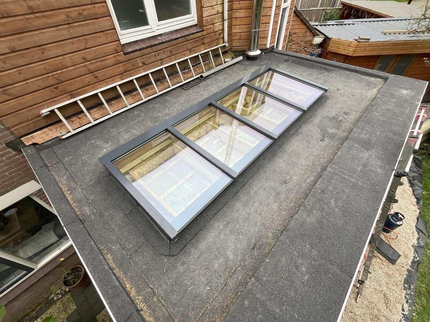 Lichtkoepels op een plat dak tegen een woonhuis, netjes ingewerkt in de dakbedekking.