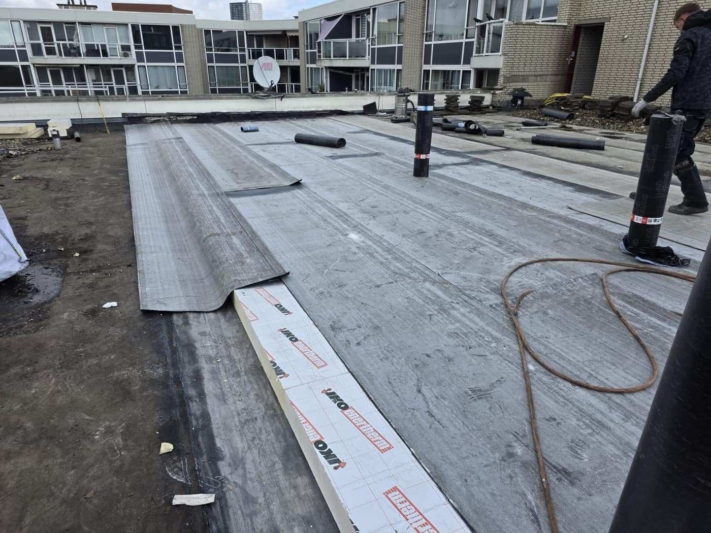 Nieuwe bitumenbanen uitgerold naast het oude dakvlak tijdens een renovatie.